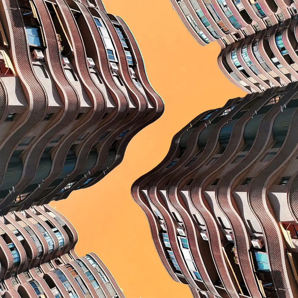 Fotomontaje de dos edificios de fachadas onduladas enfrentados en espejo sobre un cielo naranja.